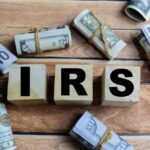 Wooden blocks spelling IRS surrounded by rolled currency notes