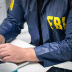 Person in FBI jacket working on laptop.