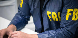 Person in FBI jacket working on laptop.