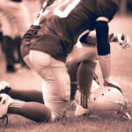 Football player kneeling on the field with a helmet beside them