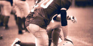 Football player kneeling on the field with a helmet beside them