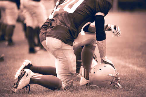 Football player kneeling on the field with a helmet beside them