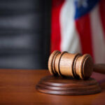 PIPE BOMB Case Explodes — More Charges A wooden gavel resting on a sound block with an American flag in the background