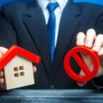 Dimon Warns: Iran War Could CRUSH Homeownership Businessman holding house model and prohibition sign