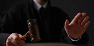 Judge holding gavel, hand raised in courtroom.