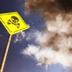 A yellow warning sign with a skull and crossbones against a cloudy sky