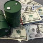 Two green oil barrels placed on a pile of hundred dollar bills