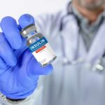 A healthcare professional holding an insulin vial in a gloved hand