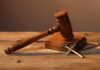 A wooden gavel resting on a block next to a cross necklace