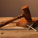 A wooden gavel resting on a block next to a cross necklace
