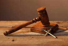 A wooden gavel resting on a block next to a cross necklace