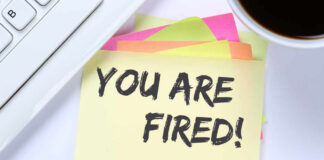 A sticky note with the message 'YOU ARE FIRED' placed on a desk next to a keyboard and a cup of coffee