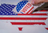 Supreme Court EXPLODES Over Voting Map Fight Hand placing a 'VOTED' sticker into a ballot box shaped like the United States