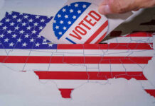Supreme Court EXPLODES Over Voting Map Fight Hand placing a 'VOTED' sticker into a ballot box shaped like the United States
