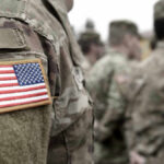Shock Pentagon Move: Troops Cut Where? U.S. soldiers in camouflage uniforms with American flag patch.