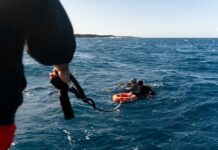 Two scuba divers in the ocean being assisted by a person holding a rescue line