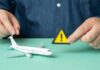 Voluntary Departures of Illegals Surging Under Trump A person holding a warning sign next to a model airplane