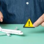 Voluntary Departures of Illegals Surging Under Trump A person holding a warning sign next to a model airplane