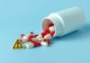 Spilled red and white capsules next to a warning sign