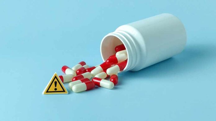 Spilled red and white capsules next to a warning sign
