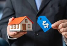 A person in a suit holding a miniature house and a price tag