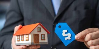 A person in a suit holding a miniature house and a price tag