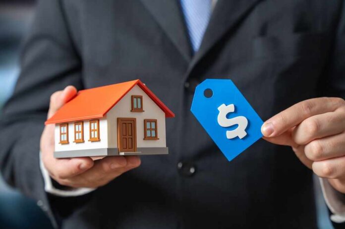 shutterstock_2708529611.jpg A person in a suit holding a miniature house and a price tag