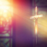 Crucifix with sunlight, stained glass window in background.