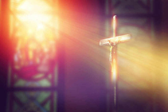 Crucifix with sunlight, stained glass window in background.