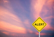 Yellow alert sign against a colorful sunset sky