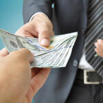 Bribery Bombshell Rocks Former Mayor’s Inner Circle A person handing over a stack of cash to another individual in a suit
