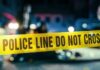 VIDEO: Midnight Raiders Slaughter 12, Injure More Police line caution tape at a crime scene with blurred figures in the background