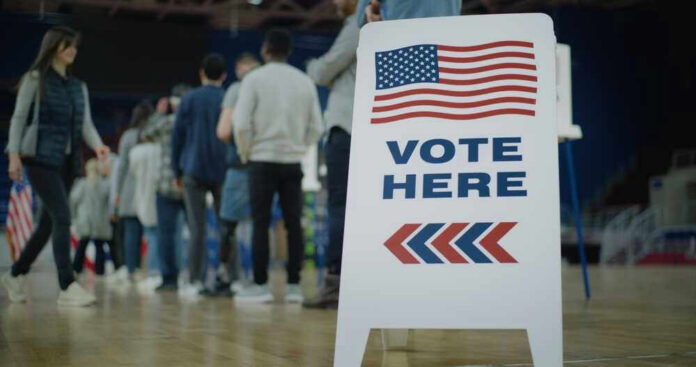 shutterstock_2454758105-1 People in line next to Vote Here sign