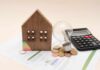 Savings Collapse Sparks Late‑Cycle Jitters A wooden house model, light bulb, coins, and a calculator on financial documents