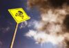 Yellow skull and crossbones warning sign against smoky sky