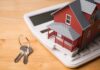 Wall Street Hit: Housing Shock Incoming? A miniature red house on a calculator with keys nearby