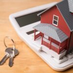 Wall Street Hit: Housing Shock Incoming? A miniature red house on a calculator with keys nearby