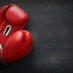 Red boxing gloves on a dark, textured surface.
