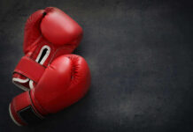 Boxing Pro Killed After Shocking Attack Red boxing gloves on a dark, textured surface.