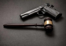 Gun Bans Go On Trial At SCOTUS Pistol and judge's gavel on dark surface