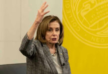 Nancy Pelosi gestures while speaking in front of yellow backdrop.