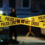 Deadly Chaos: Six Down, No Answers Police tape marking a crime scene with blurred figures in the background