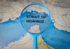Hormuz Shock Slams Farm Costs Magnifying glass highlighting the Strait of Hormuz on a map