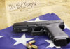 Federal Gun Rules Gutted Overnight A handgun resting on an American flag with bullets and a historical document in the background