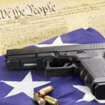 Federal Gun Rules Gutted Overnight A handgun resting on an American flag with bullets and a historical document in the background