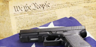 A handgun resting on an American flag with bullets and a historical document in the background