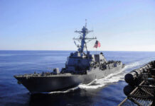 Warship with American flag sailing in the ocean.