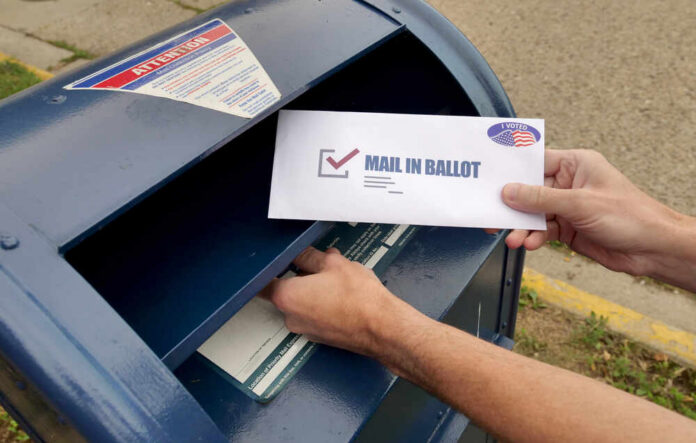 Circa,August,,2020,-,A,Man,Puts,An,Absentee,Mail-in Hands mailing a ballot envelope into a blue mailbox