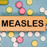 Wooden block with the word 'MEASLES' surrounded by various pills