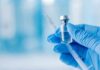 A gloved hand holding a syringe and a vial of liquid